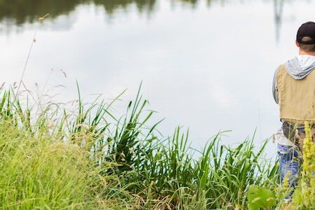A fisherman with a fishing rod fishes peacefully at a calm pond.