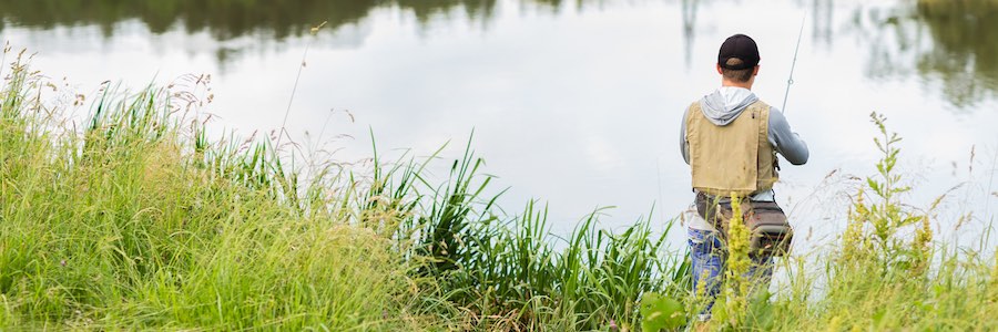 A fisherman with a fishing rod fishes peacefully at a calm pond.